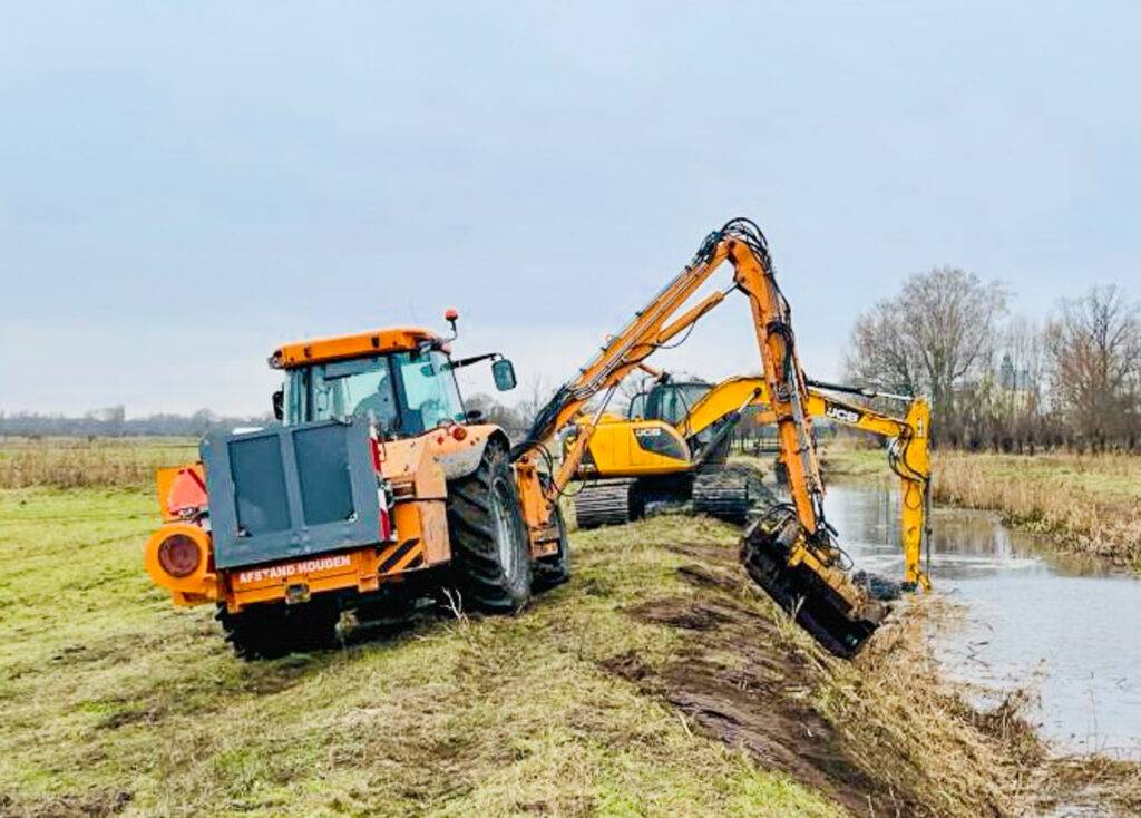 Ciągnik Massey Ferguson z kosiarką Herder na wysięgniku 10 m podczas koszenia skarpy wzdłuż kanału.