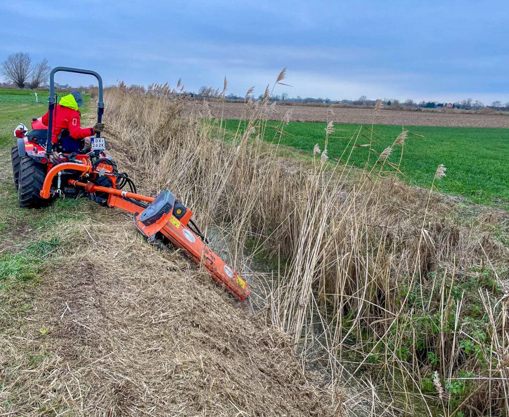 Mulczowanie skarpy rowu przy użyciu kosiarki ramieniowej zamontowanej na małym ciągniku – prace przy linii brzegowej.Mulczowanie skarpy rowu przy użyciu kosiarki ramieniowej zamontowanej na małym ciągniku – prace przy linii brzegowej.